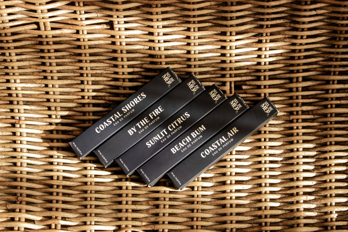 Coastal Shores fragrance boxes arranged diagonally on a woven wicker surface. Visible scents include Coastal Shores, By the Fire, Sunlit Citrus, Beach Bum, and Coastal Air.